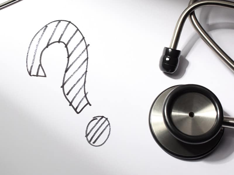 A question mark is drawn on a doctor's clipboard with stethoscope.