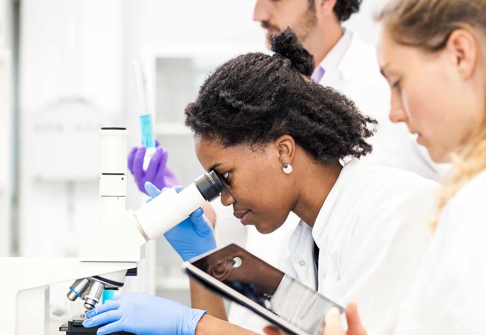 woman looking into microscope while co-worker looks at EHR