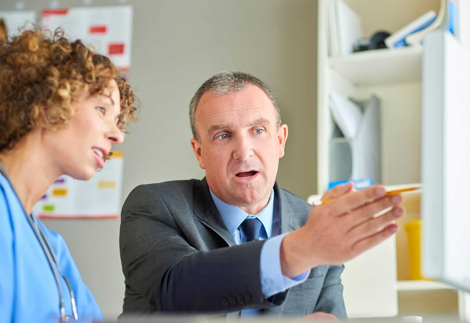 Business person explaining value based care requirements on a computer to a doctor.