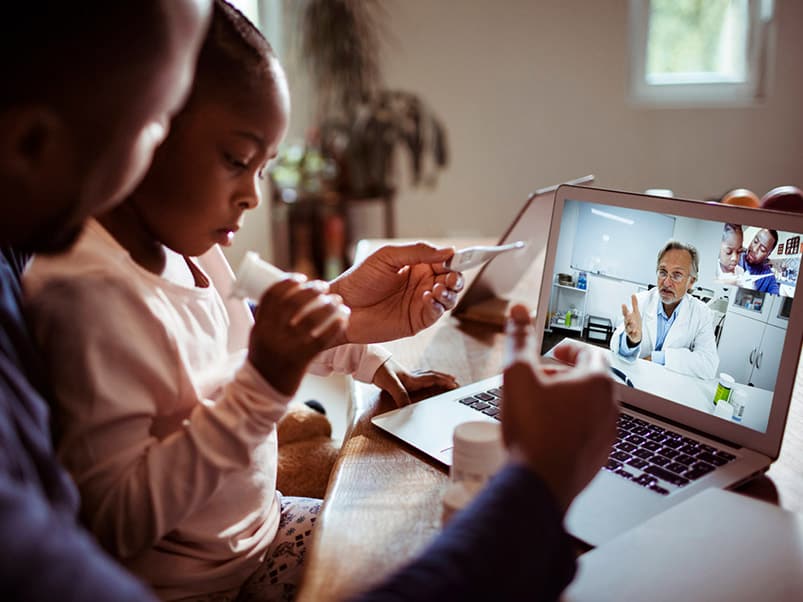 A father holding his daughter during a telehealth visit with a doctor.