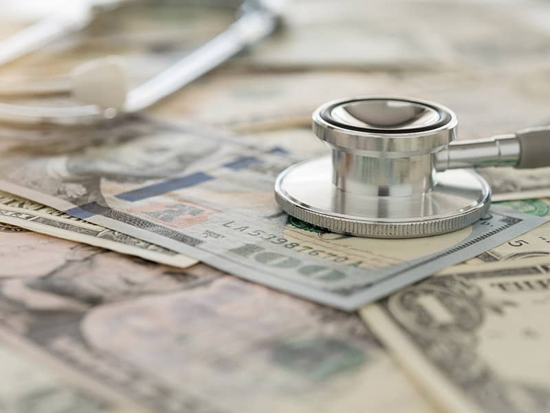 A stethoscope on top of dollar bills representing money insurance companies pay for medical care.