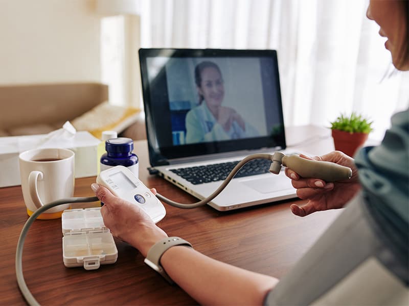 Woman on a virtual call with her physician while measuring her blood pressure, representing RPM EHR integration.